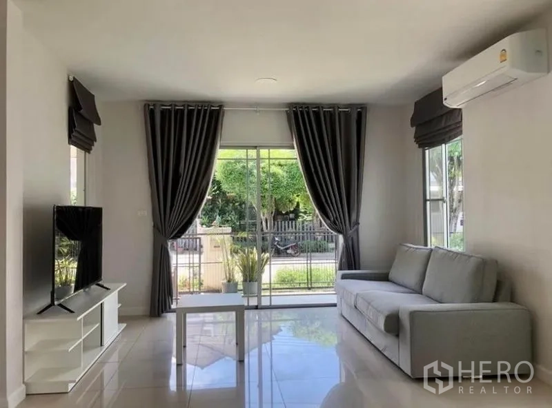 บ้าน ให้เช่าในPrawet, Bangkok - ห้องนั่งเล่นสว่าง โซฟาสีเทา ชั้นวางทีวี และประตูกระจกบานเลื่อนออกสู่สวน