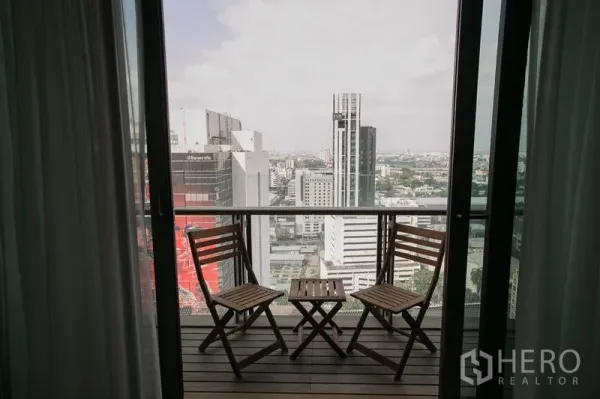 公寓 出租或出售在Watthana, Bangkok - 高楼阳台，两把木椅与小桌，远眺曼谷城市天际线。