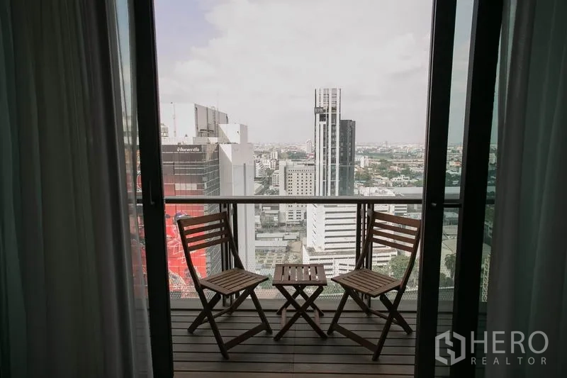 公寓 出租或出售在Watthana, Bangkok - 高楼阳台，两把木椅与小桌，远眺曼谷城市天际线。