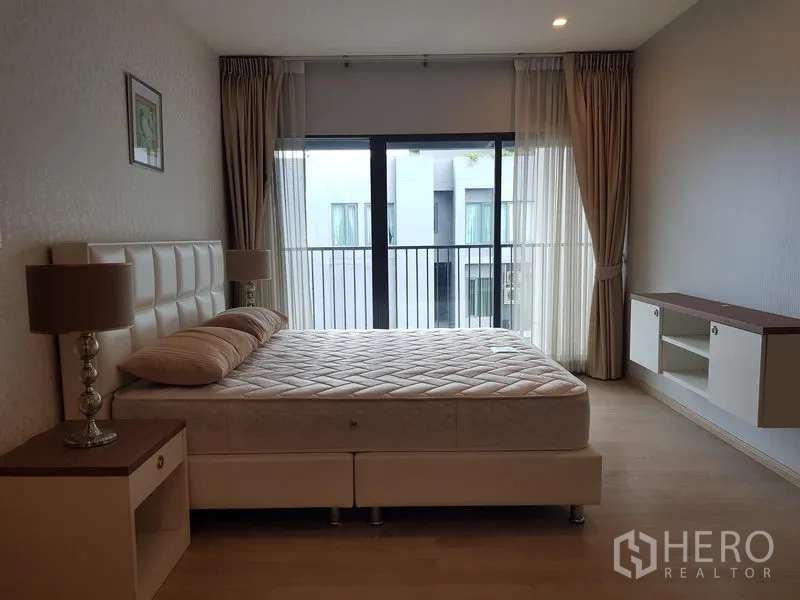Condominium for rent in Khlong Toei, Bangkok - Second bedroom with upholstered bed, bedside tables and floor-to-ceiling windows.