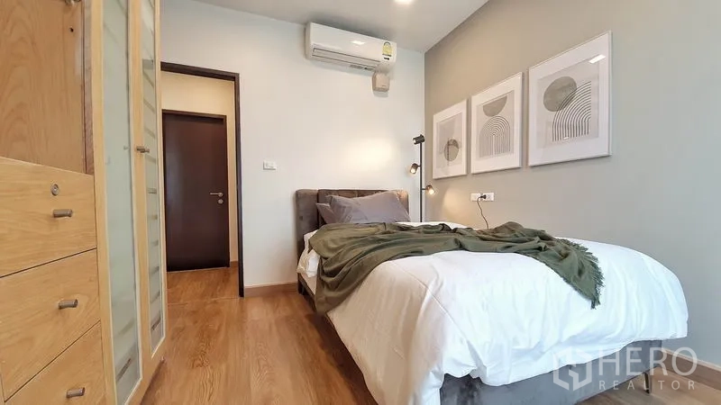 Condominium for rent in Khlong Toei, Bangkok - Second bedroom with single bed, artwork, air conditioner and wardrobe on warm timber flooring.