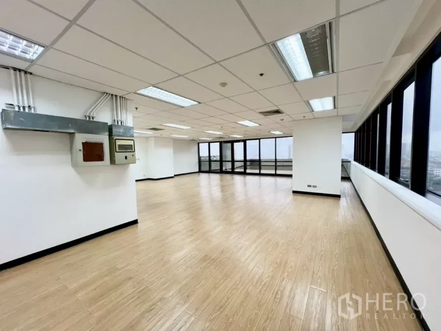 办公空间 出租在Huai Khwang, Bangkok - 转角办公室内部，木纹地板，吊顶灯具，墙面电箱与大面积窗户。