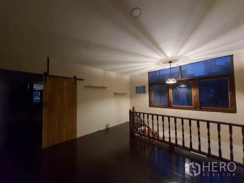 独立式住宅 出租在Pathum Wan, Bangkok - 二层楼梯厅夜景，吊灯投射光影、木扶手与谷仓门