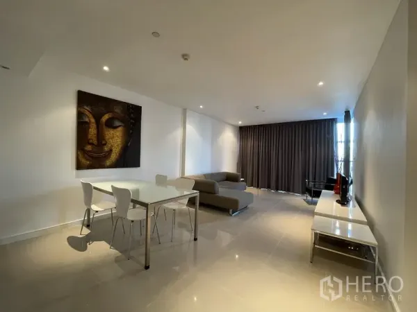 Condominium for rent or sale in Watthana, Bangkok - Dining area with glass table and four white chairs beside a modern lounge and full-length blackout curtains.