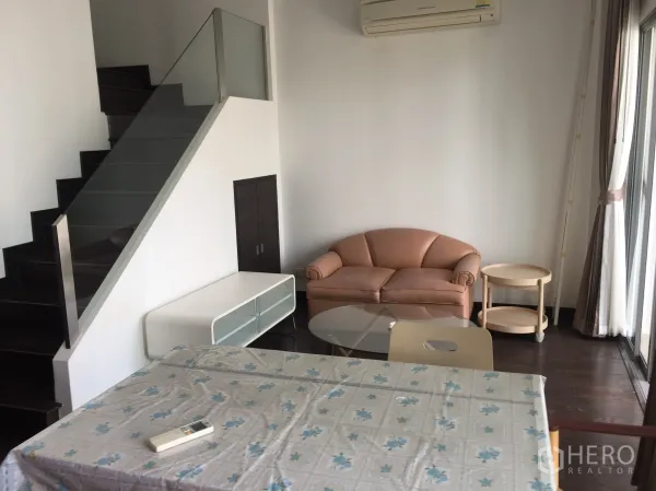 公寓 出租在Ratchathewi, Bangkok - Loft风客厅，沙发、玻璃茶几与玻璃栏杆楼梯。