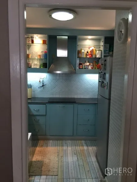 Condominium for rent or sale in Watthana, Bangkok - Enclosed kitchen with blue cabinetry, range hood, open shelving and tiled backsplash.