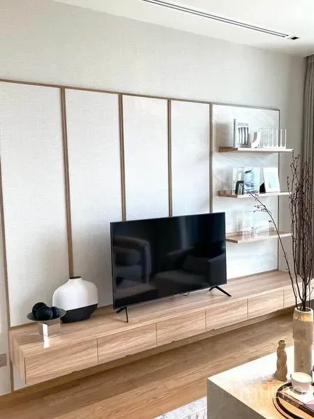 Condominium for rent or sale in Khlong Toei, Bangkok - Minimalist living room feature wall with floating TV console and open shelves in light wood.
