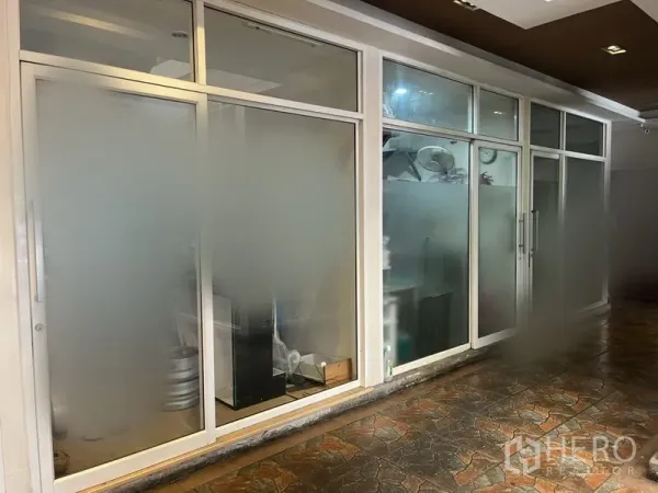 Retail Space for rent in Khlong Toei, Bangkok - Frosted-glass shopfront with white aluminum frames and a sliding door along a covered tiled walkway.
