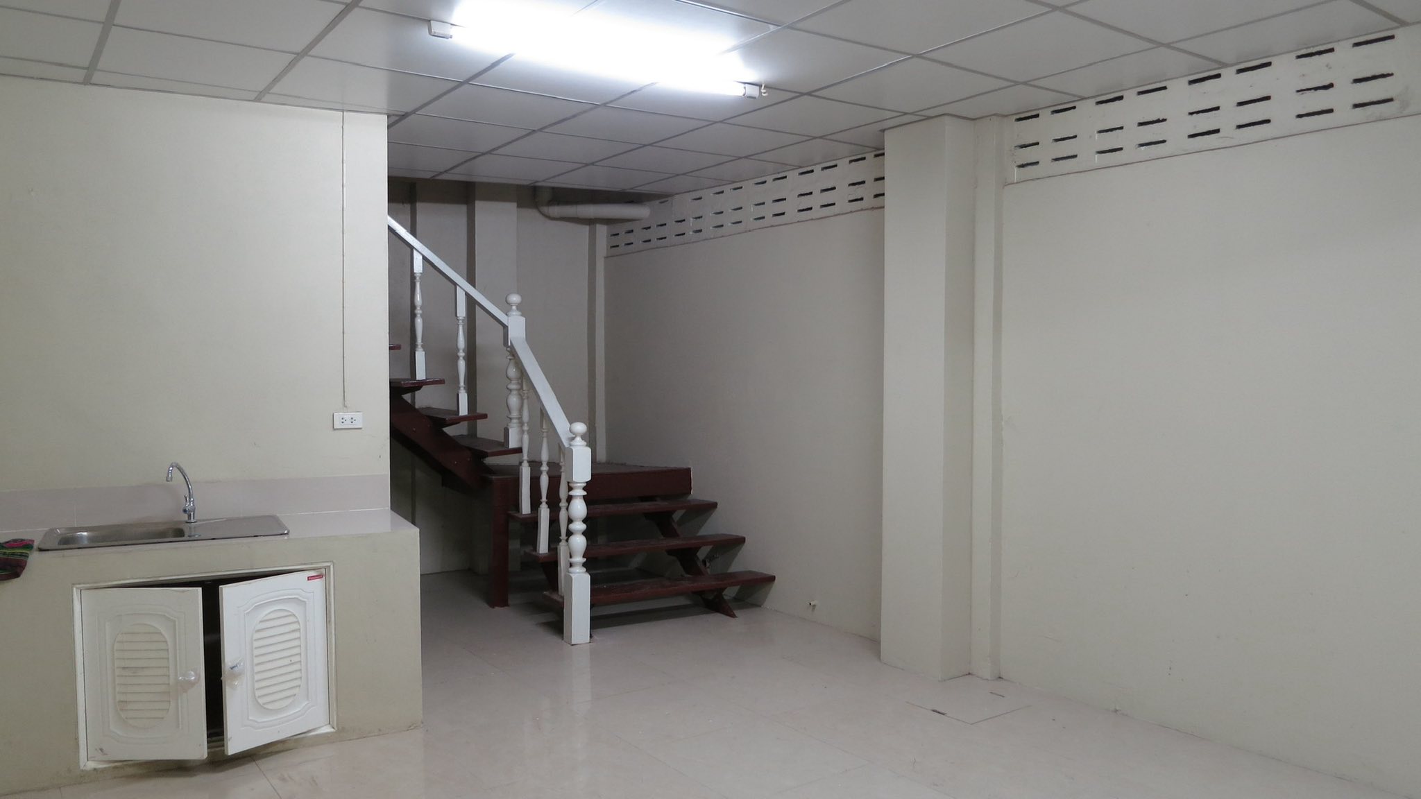 Warehouse for rent in Wang Thonglang, Bangkok - Compact kitchenette and wooden staircase in the warehouse office area with tiled floor and drop ceiling.