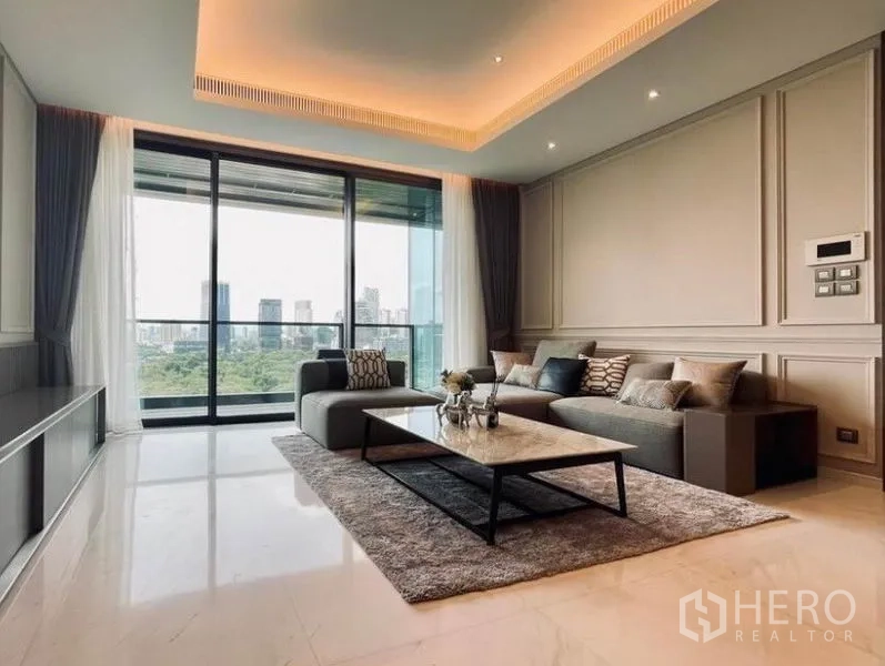公寓 出租在Pathum Wan, Bangkok - 宽敞客厅配L型沙发与氛围灯，通过落地玻璃门欣赏城市天际线。