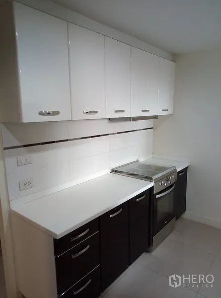 Condominium for rent in Watthana, Bangkok - Fitted kitchen with ample white cabinetry, long countertop, and electric oven.
