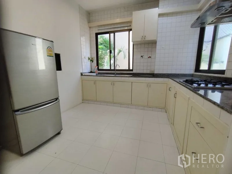 Detached House for rent in Watthana, Bangkok - L-shaped kitchen with granite counters, windows, and stainless refrigerator.