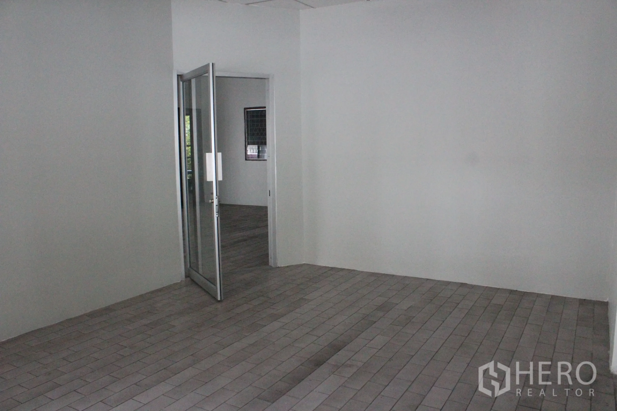 Home Office for rent in Khlong Toei, Bangkok - Clean tiled lobby or office room with white walls and an open glass door leading to another room.
