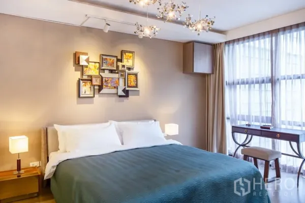Condominium for rent in Watthana, Bangkok - Cozy bedroom with king bed, decorative wall art, stylish chandeliers, and large windows with writing desk.