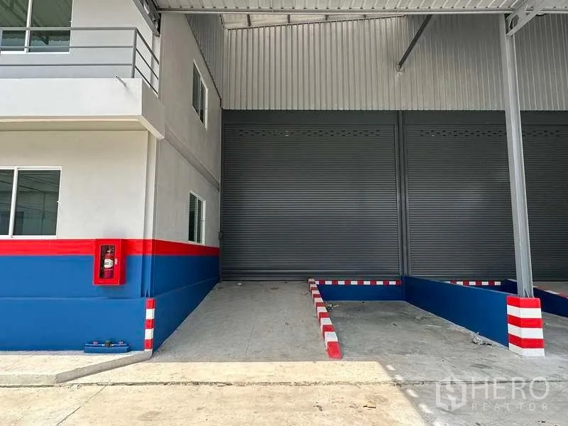 货栈 出租在Samut Prakan - 近景：遮雨装卸区，卷帘门、导向护栏和消防箱
