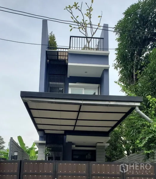 独立式住宅 出租在Watthana, Bangkok - 现代三层独栋住宅，带屋顶露台、带顶车位与高门围栏，周围绿树环绕。