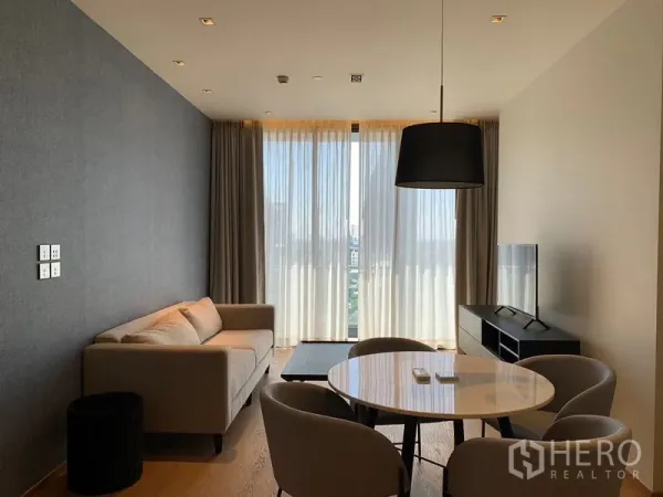Condominium for rent in Khlong Toei, Bangkok - Bright living and dining area with sofa, round table, pendant light, and floor-to-ceiling windows with city view.