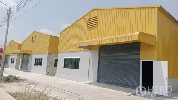 คลังสินค้า ให้เช่าในNonthaburi - โกดังหลังคาเหลืองเรียงกัน ประตูม้วนขนาดใหญ่ พร้อมถนนคอนกรีตหน้าอาคารในปากเกร็ด นนทบุรี