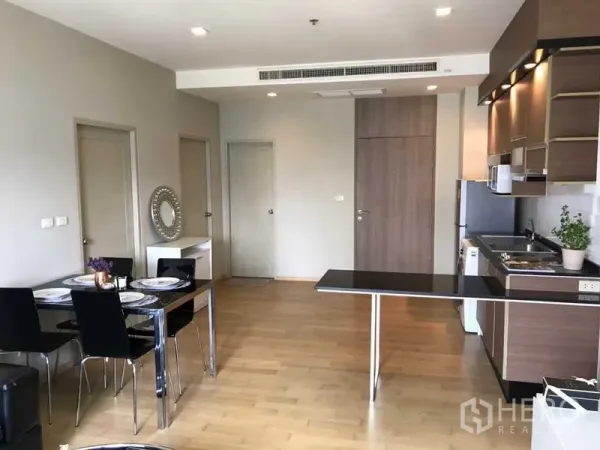 公寓 出租在Watthana, Bangkok - 四人餐区，旁有加长吧台与浅色木地板的全套厨房