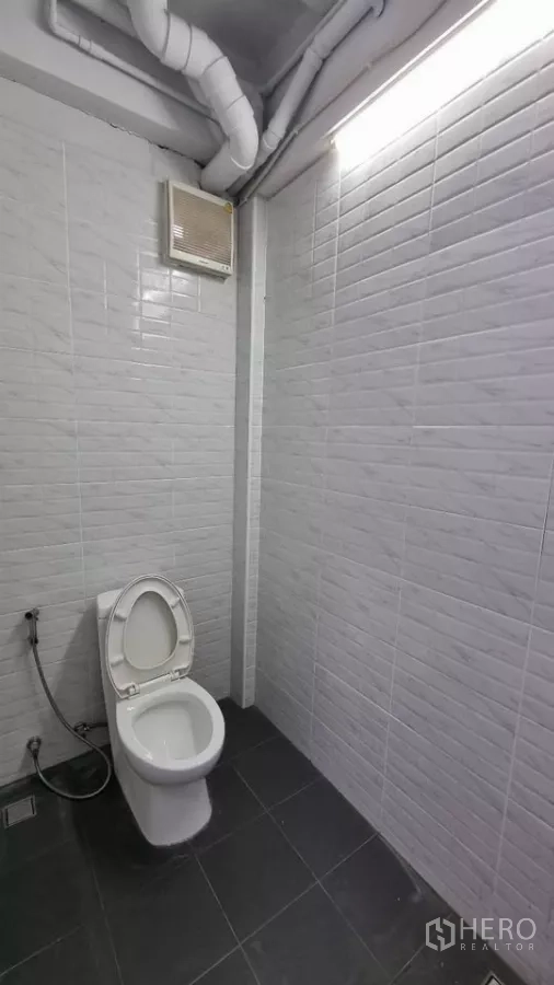 Townhouse for rent in Huai Khwang, Bangkok - Bathroom with white wall tiles, dark floor tiles and an exhaust fan.