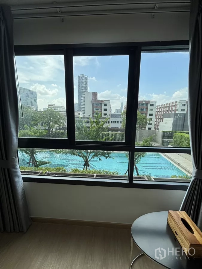 公寓 出租在Phra Khanong, Bangkok - 窗外可见长条泳池、绿树与低密度天际线。