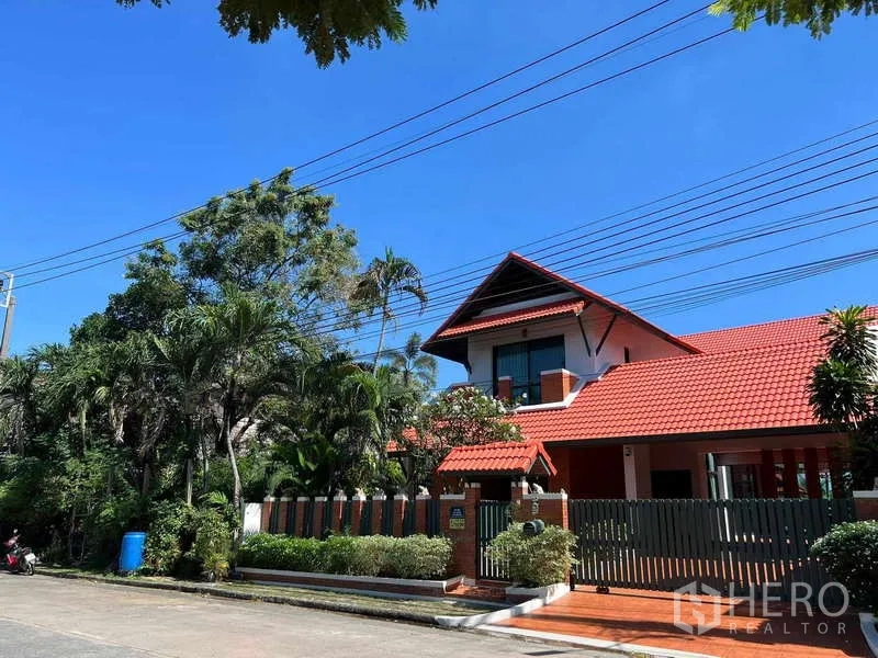 Detached House for rent in Bang Phli, Samut Prakan - Street view of a two-storey detached house with red tiled roof, brick exterior and gated fence amid greenery in Bang Phli.