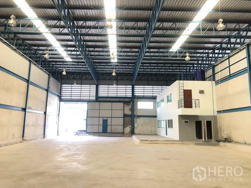 Warehouse for rent in Bang Phli, Samut Prakan - Interior view showing large shutter door, bright lighting and attached two‑storey office block.