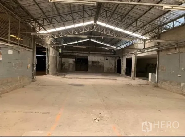 Warehouse for rent in Samut Prakan - Spacious warehouse interior with high steel truss roof, skylight panels, and multiple loading doors.