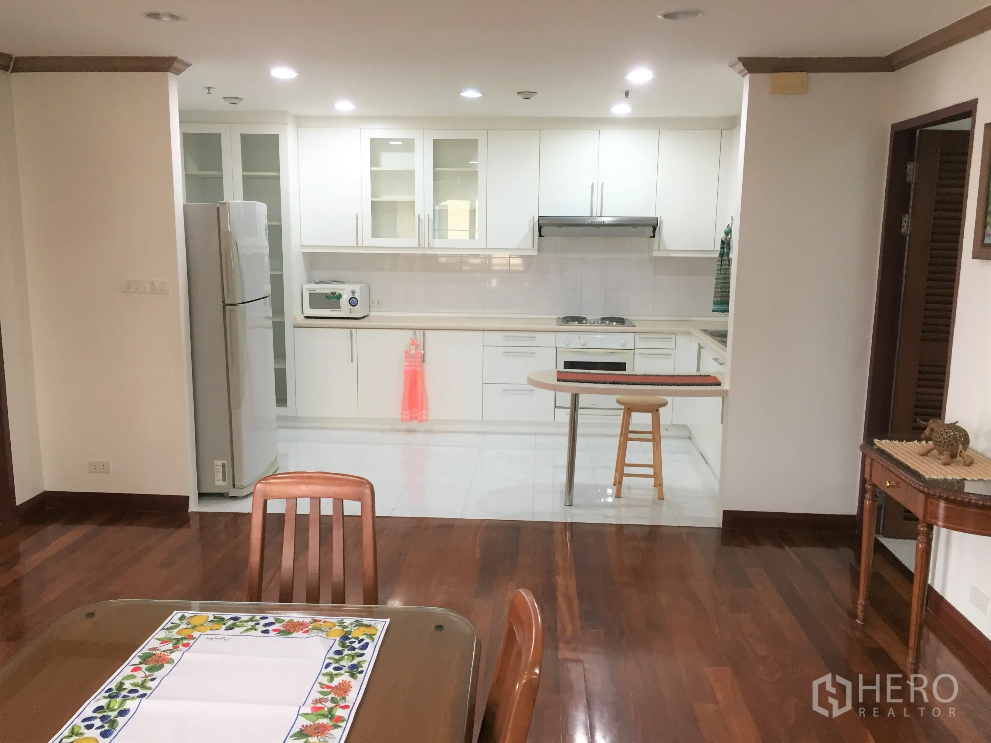 คอนโด ให้เช่าในWatthana, Bangkok - ครัวเปิดโทนสีขาวพร้อมเคาน์เตอร์บาร์ ตู้กระจก และพื้นที่รับประทานอาหารพื้นไม้