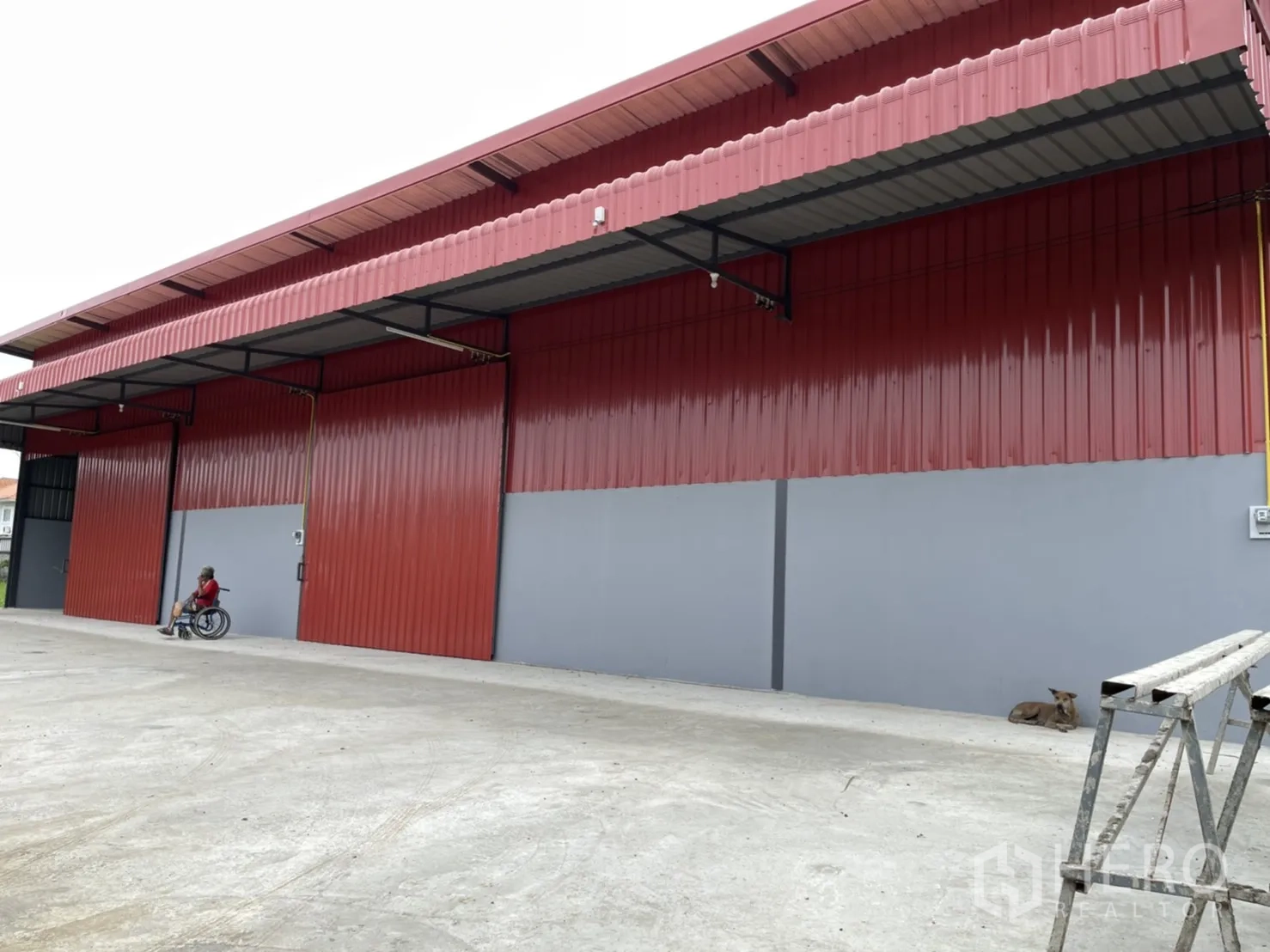 Factory for rent in Khlong Luang, Pathum Thani - Exterior of red metal-clad warehouse with wide driveway and loading area.