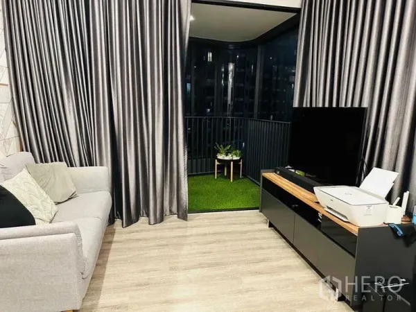 คอนโด ให้เช่าในHuai Khwang, Bangkok - ห้องนั่งเล่นมีชั้นวางทีวี เปิดออกสู่ระเบียงปูหญ้าเทียม