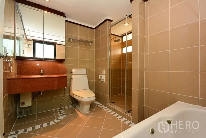 Apartment for rent in Khlong Toei, Bangkok - Modern bathroom with glass-enclosed shower, bathtub, mirrored cabinets and tiled walls.