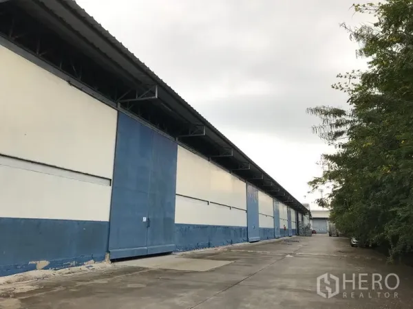 货栈 出租在Bang Phli, Samut Prakan - 蓝白色仓库外立面，宽阔混凝土车道与装卸区，位于邦普里。