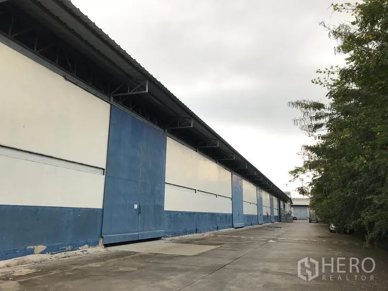 Warehouse for rent in Bang Phli, Samut Prakan - Long blue-and-white warehouse exterior with a wide concrete driveway and loading access in Bang Phli.