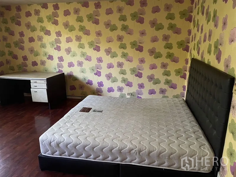 Home Office for rent in Watthana, Bangkok - Bedroom with floral wallpaper, wood flooring, upholstered bed and a corner desk.