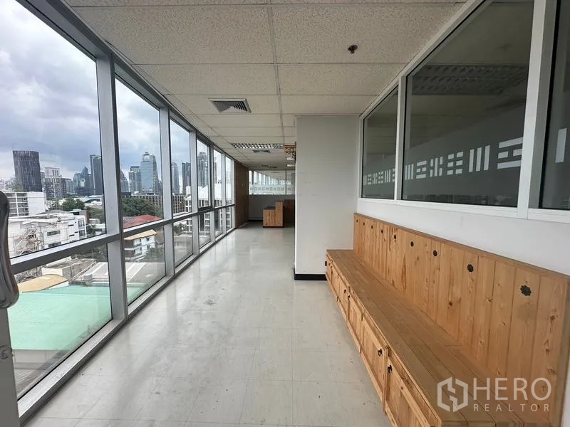 Office Space for rent - Long corridor-style workspace lined with full-height windows and built-in wooden bench seating.