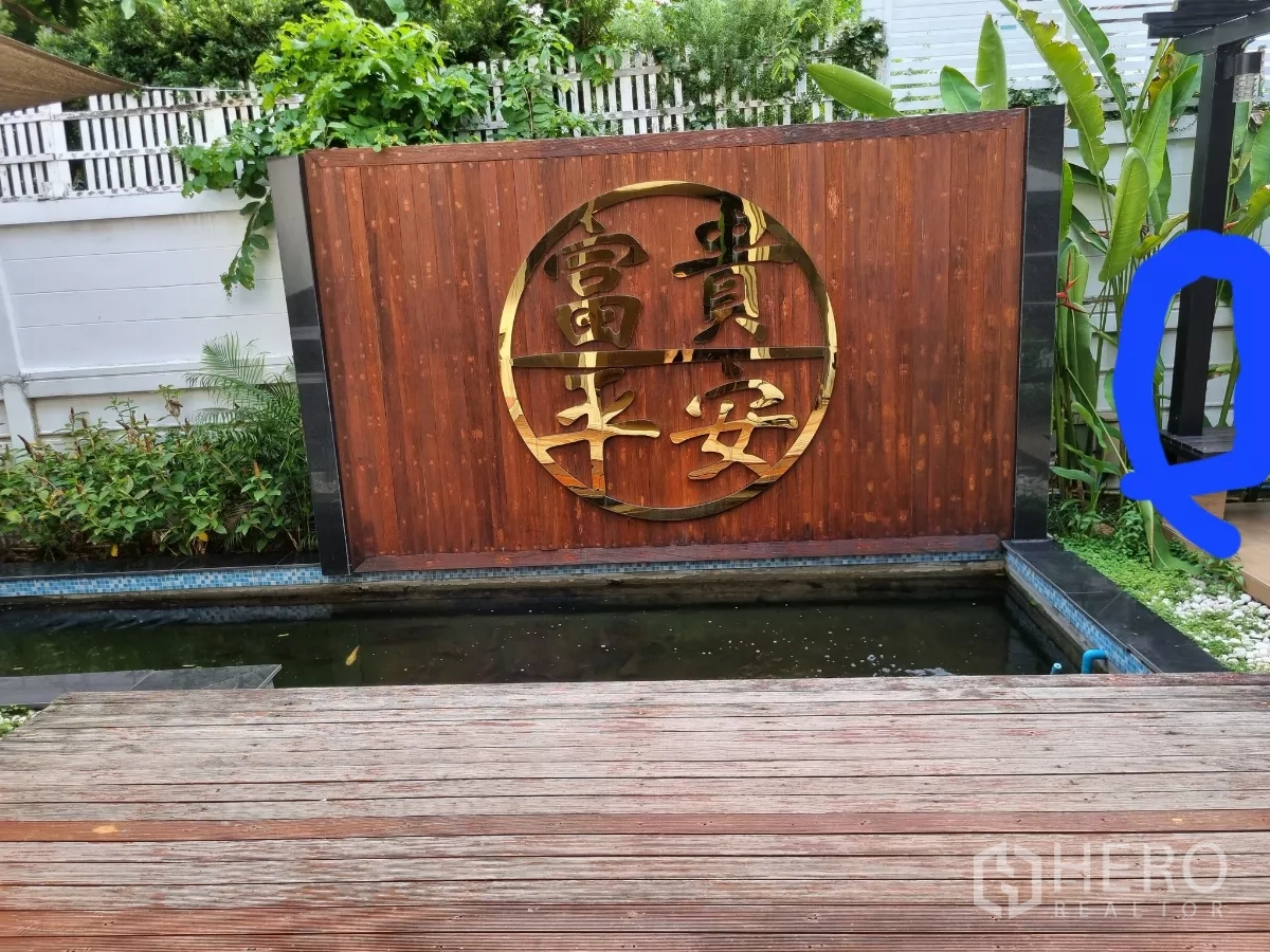 独立式住宅 出租在Bang Kapi, Bangkok - 木平台旁的锦鲤池与金色圆形图案景墙。