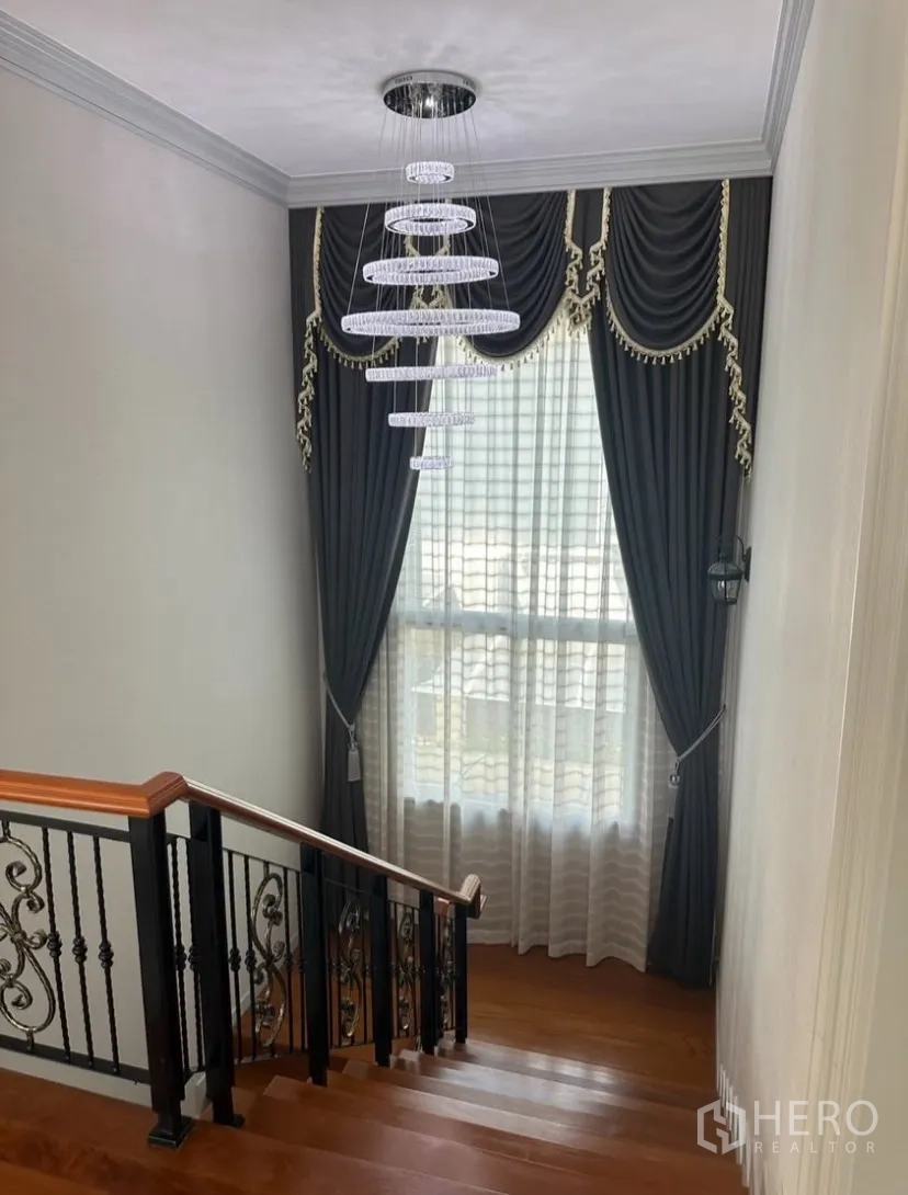 Detached House for rent or sale in Prawet, Bangkok - Staircase with polished wooden steps, wrought-iron balustrade, and a modern ring chandelier.