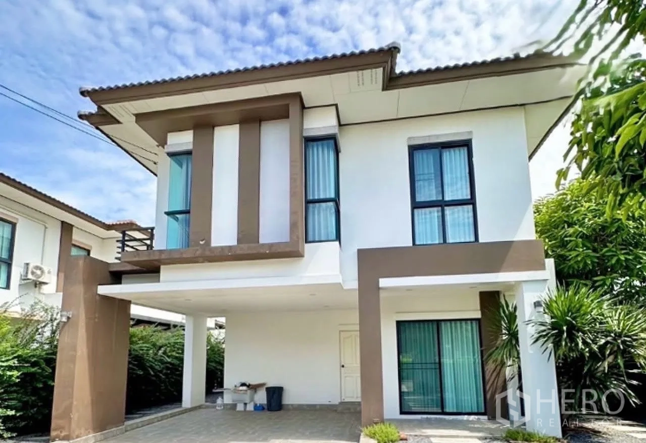 Detached House for sale in Lam Luk Ka, Pathum Thani - Close view of the house exterior showing carport, tall windows with curtains and white-and-brown facade.