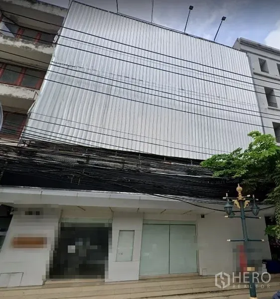 Shophouse for rent or sale in Watthana, Bangkok - Street view of a multi-storey shophouse exterior with a wide glass storefront and metal cladding.