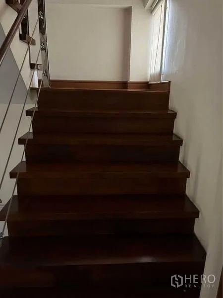 Townhouse for sale in Phra Khanong, Bangkok - Wood staircase with metal railing and a side window leading to upper levels.