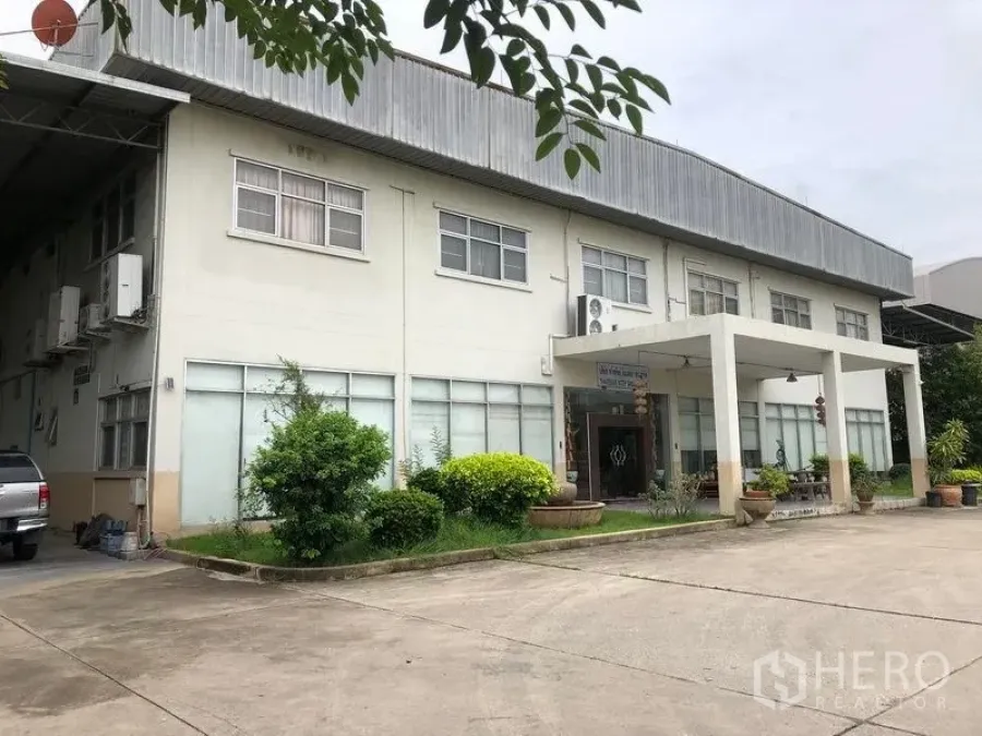 Factory for rent or sale in Lam Luk Ka, Pathum Thani - Close-up of the office façade with a covered entrance, windows and landscaped greenery.