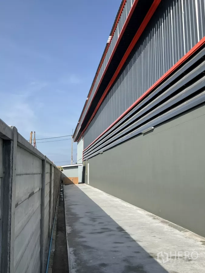 Factory for sale in Samut Sakhon - Rear service lane along the exterior wall within a secure fenced site.