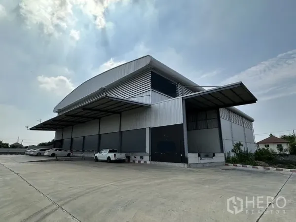 货栈 出租在Lat Krabang, Bangkok - 曼谷叻甲挽现代钢结构仓库外观，带大面积遮雨装卸月台、多扇卷闸门与宽阔混凝土场地，便于卡车进出。