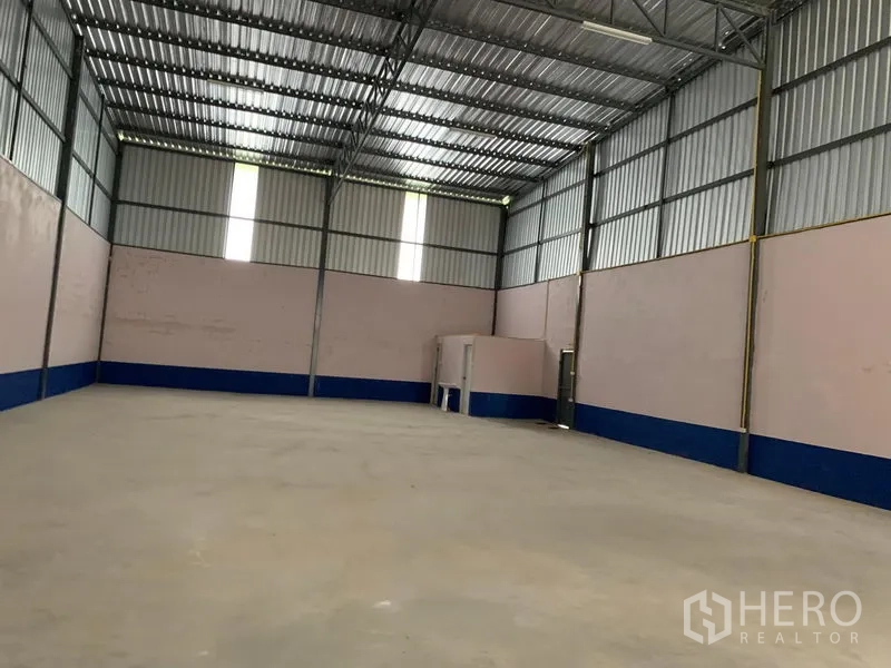 Warehouse for rent in Saphan Sung, Bangkok - Wide clear-span warehouse interior showing ventilation windows, concrete slab, and a small built-in room at the rear.