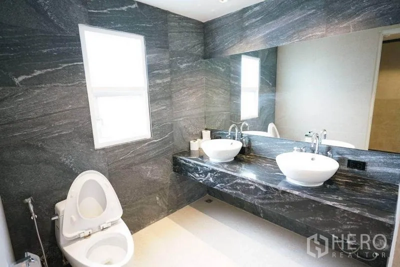 Condominium for rent or sale in Bang Na, Bangkok - Bathroom with dark marble walls, wide countertop, twin vessel sinks and large mirror.