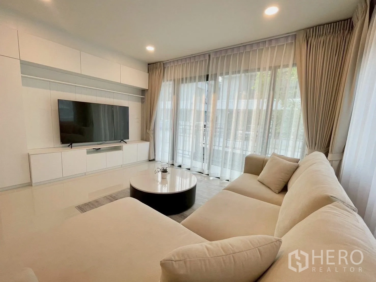 Detached House for rent in Bang Phli, Samut Prakan - Lounge with large beige sectional sofa, TV wall unit, and full-height curtains.