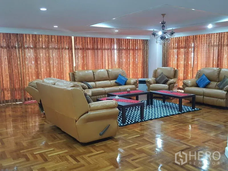公寓 出租在Watthana, Bangkok - 超大客厅，棕色真皮沙发组，吊灯，落地窗帘与拼花木地板。