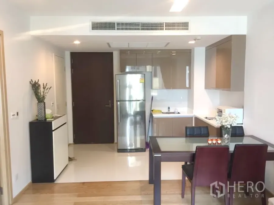 Condominium for rent in Khlong Toei, Bangkok - Open-plan kitchen and dining with glossy cabinets, stainless fridge and a glass-top table in a modern Sukhumvit condo.