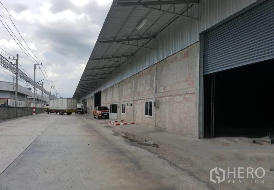 Warehouse for rent in Lam Luk Ka, Pathum Thani - Covered loading zone with trucks parked alongside the warehouse.